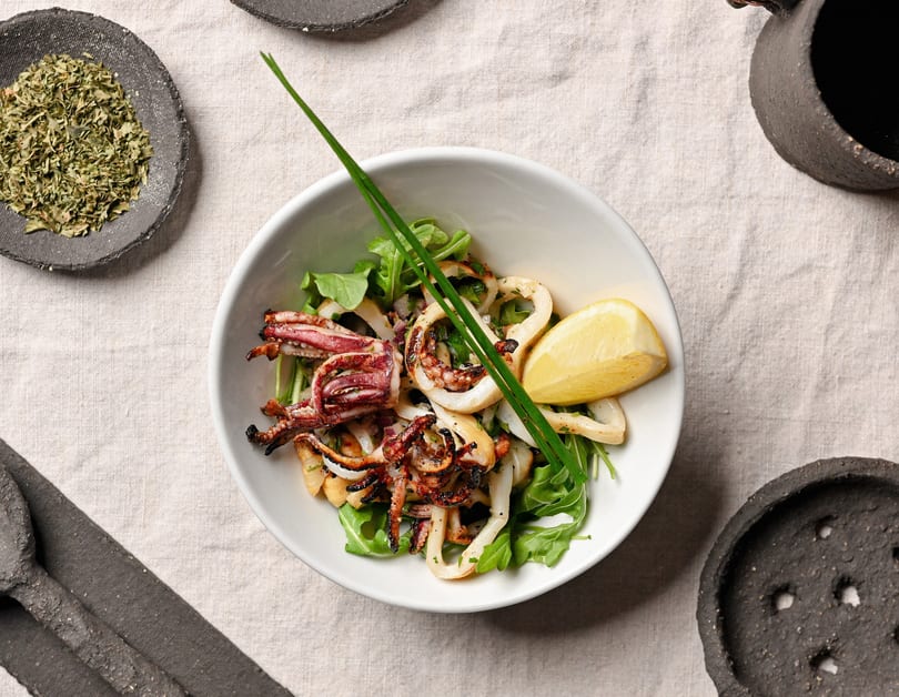 Grilled calamari and tentacles on a bed of arugula with a lemon wedge and chives.