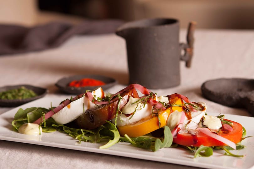 Caprese salad with sliced tomatoes, mozzarella, arugula, pickled onions, and balsamic glaze.