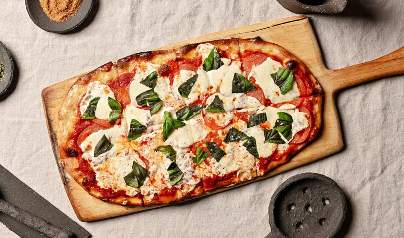 A rectangular Margherita pizza with fresh basil and mozzarella on a wooden paddle.