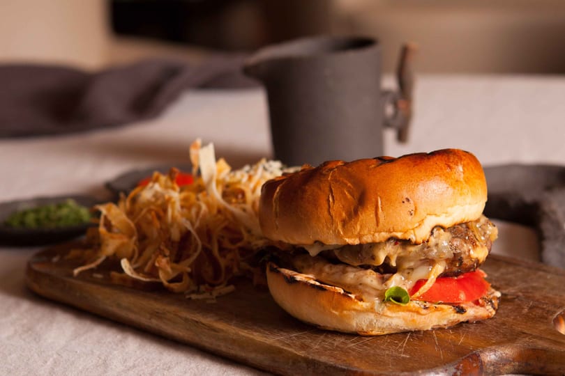 Gourmet burger with melted cheese, tomato, and lettuce, served with crispy fries on a wooden board.