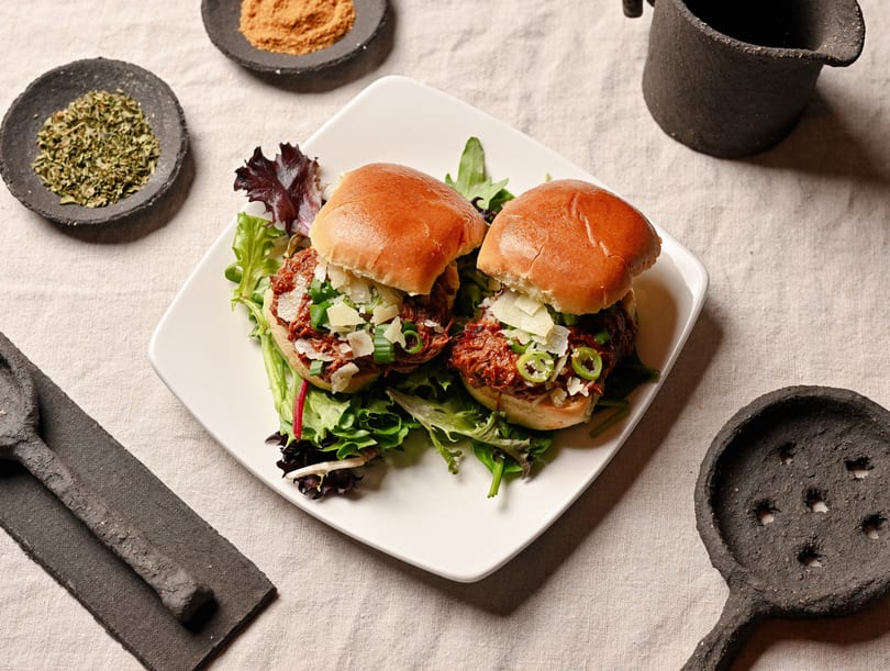 Two pulled pork sliders with cheese and green onions on a bed of lettuce.