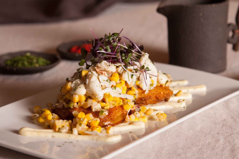 Crab and corn salad with microgreens on fried green tomatoes, drizzled with white sauce.