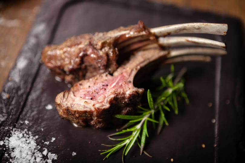 Two perfectly cooked lamb chops with rosemary and sea salt on a dark plate.