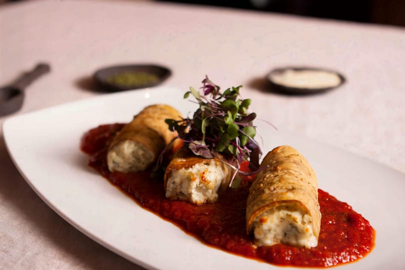 Three stuffed pasta rolls on a bed of red sauce, garnished with microgreens on a white plate.